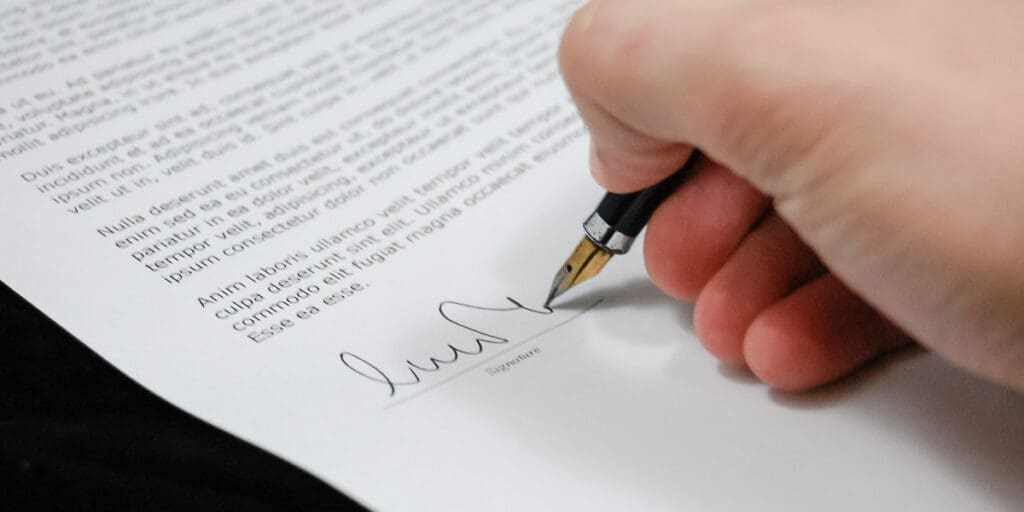 hand of a prospective apprentice signing a cover letter with a fountain pen before submitting it to a potential employer.