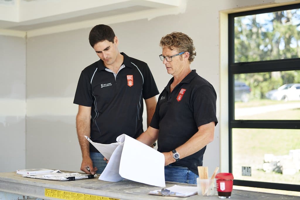 construction company boss reviewing project plans with a young builder on-site.