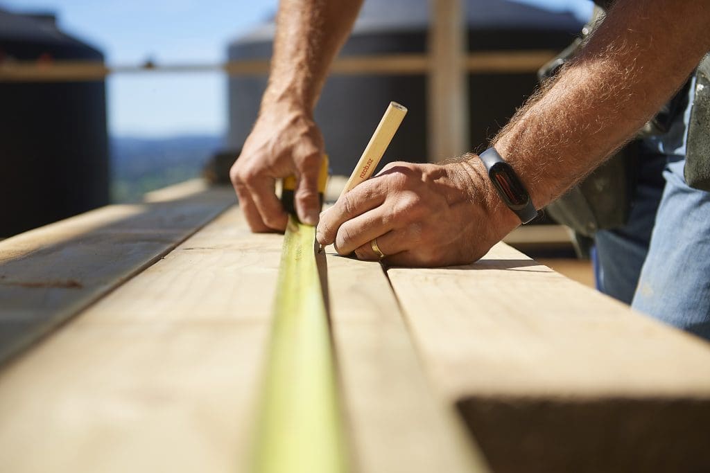 close up of a builder measuring planks of wood with a tape measure and marking where to cut with a pencil